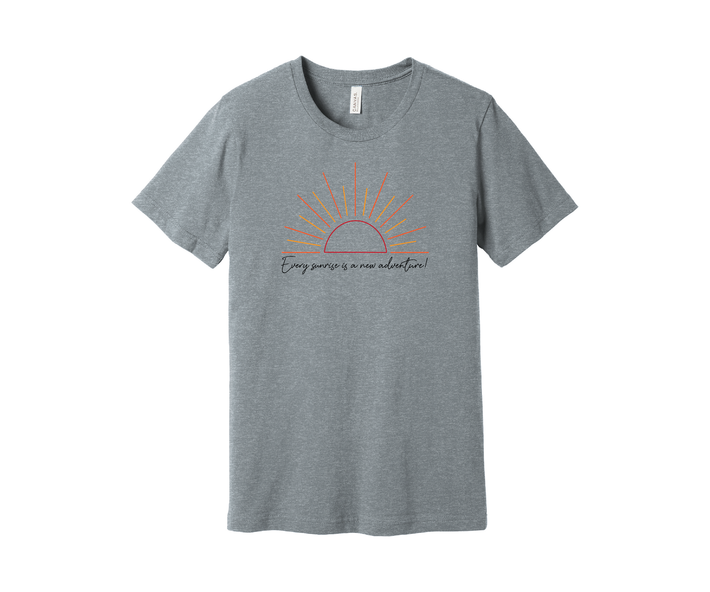 A light gray heather T-shirt features a graphic of a stylized orange and yellow sunrise above a handwritten cursive message in black that reads, "Every sunrise is a new adventure!" The shirt has a simple and modern design.