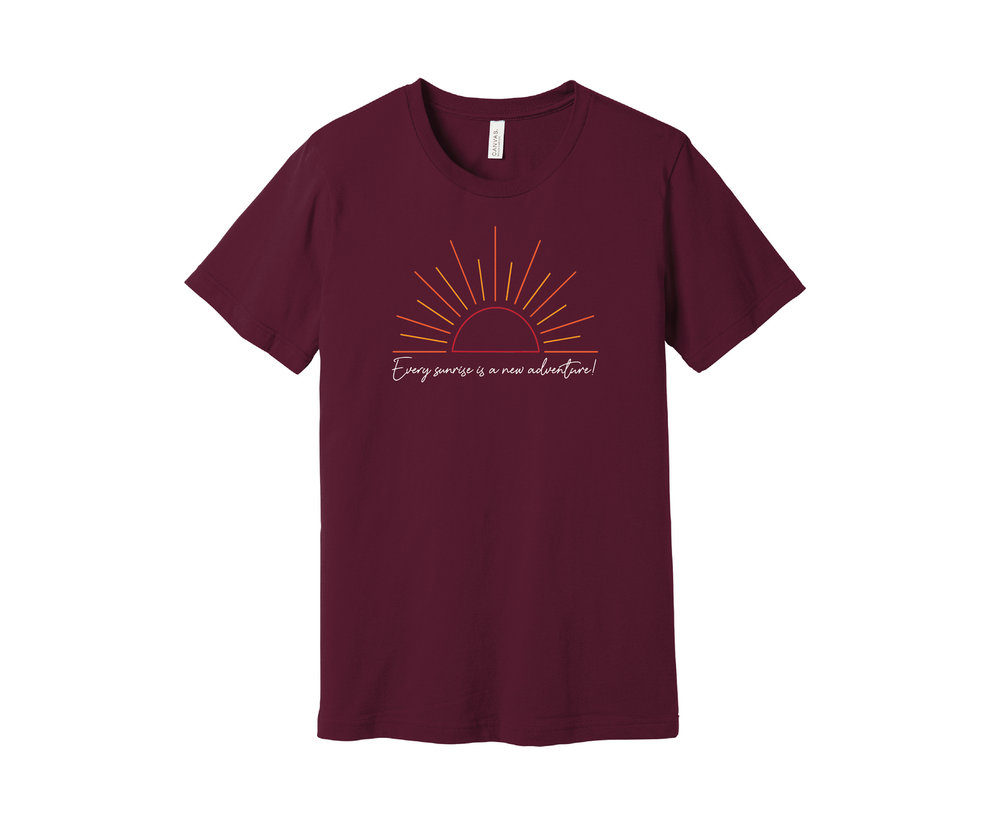 A maroon T-shirt features a graphic of a stylized orange and yellow sunrise above a handwritten cursive message in white that reads, "Every sunrise is a new adventure!" The shirt has a simple and modern design.