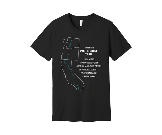 A black T-shirt displays a white map outline of the states of California, Oregon and washington and the route of the Pacific Crest Trail in teal. Text on the shirt reads: "I Hiked the Pacific Crest Trail," and lists details: 2,650 miles, 489,500 ft elevation gain, Over 60 Mountain Passes, 28 National Forests, 7 National Parks, 5 State Parks.